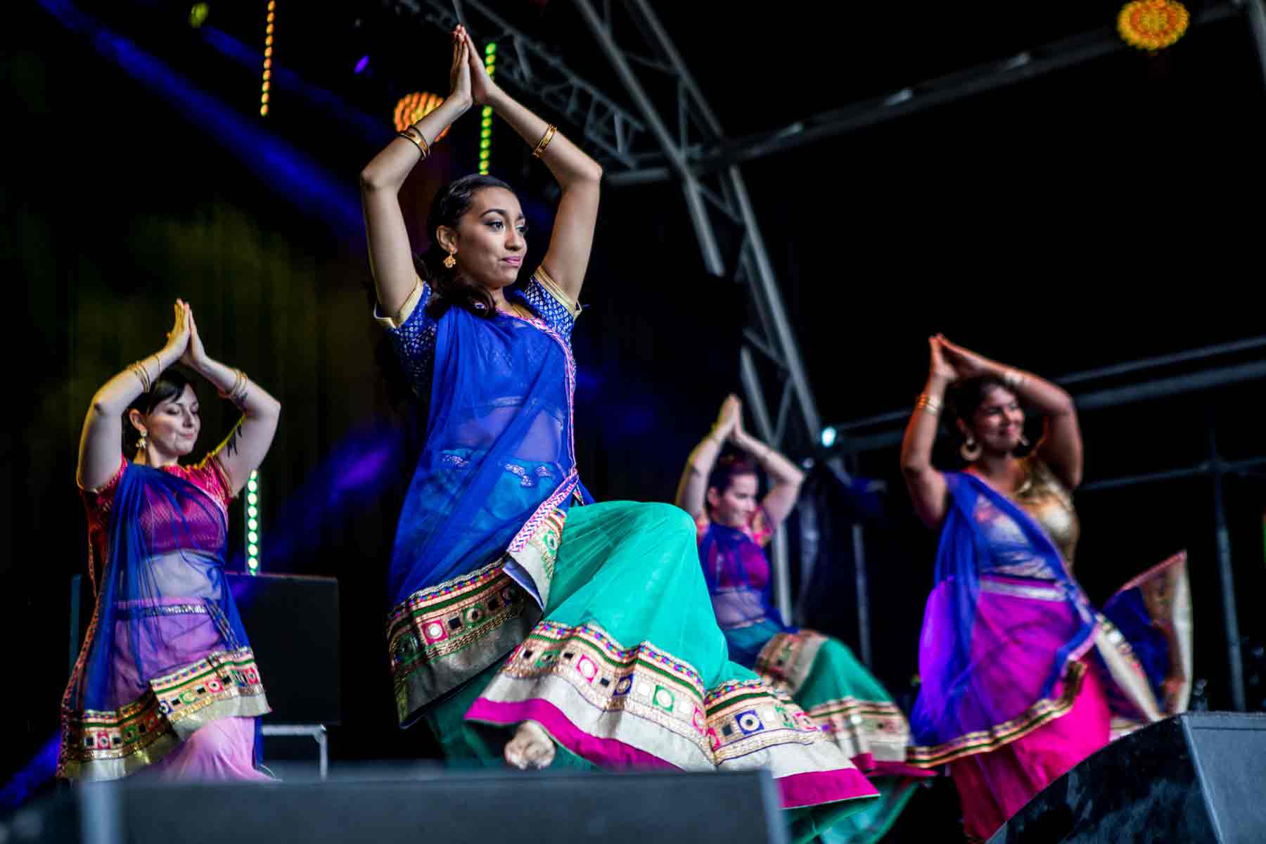 A group of dancers wearing traditional indian attire pose with their hands above their heads